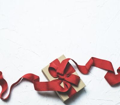 An elegant gift box with a flowing red ribbon on a textured white background, perfect for celebrations.